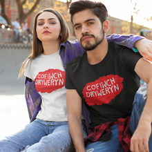Load image into Gallery viewer, Two models sitting together at a skatepark wearing matching graphic t-shirts. The model on the left wears a white t-shirt with a red paint-splatter logo containing the Welsh text 'COFIwCH DRYWERYN', and the model on the right wears a black t-shirt with the same red logo.